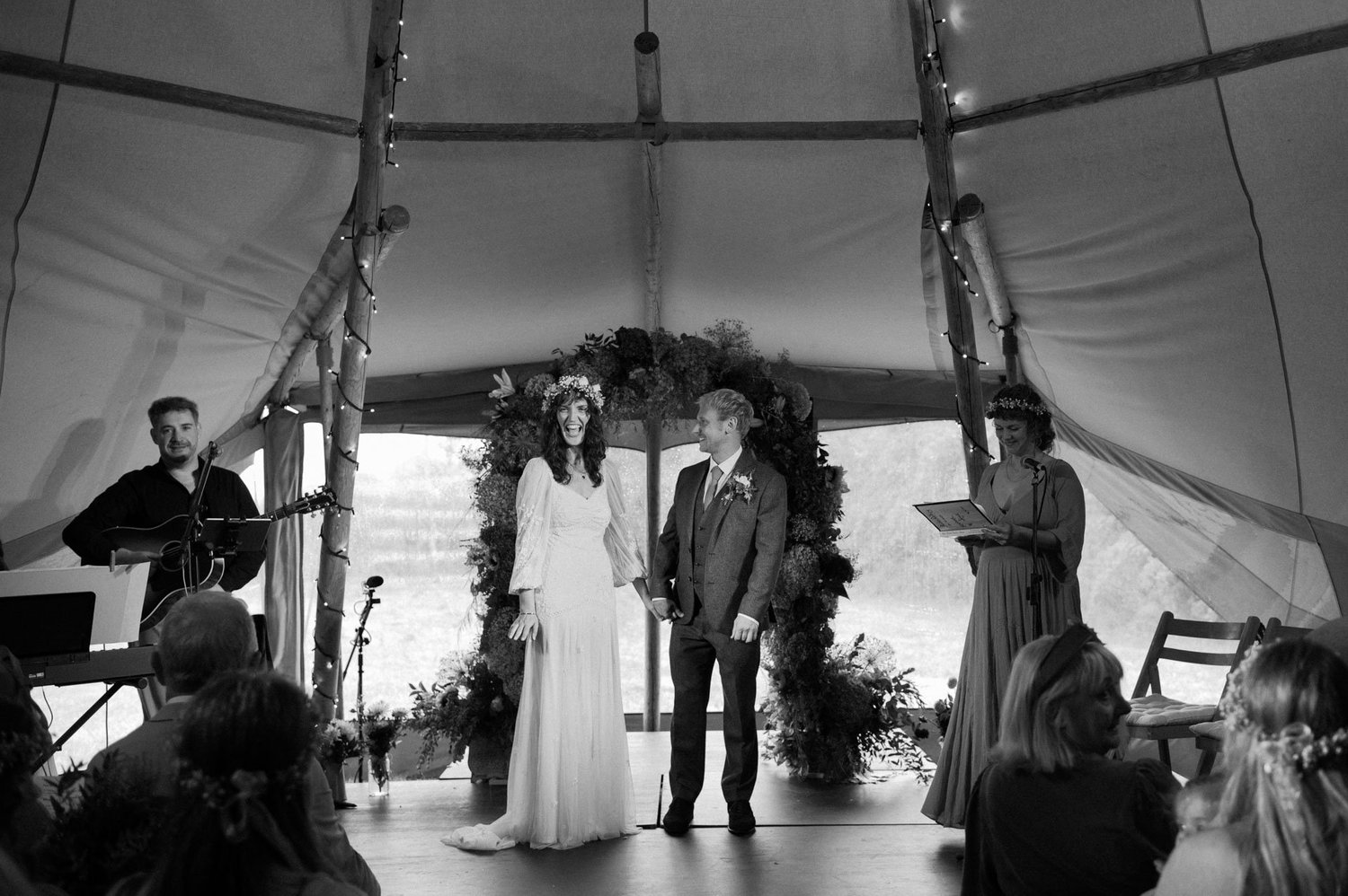 Hannah and Alex standing together beneath the floral ceremony arch