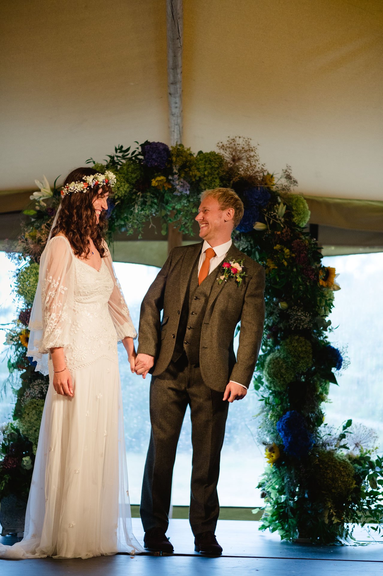 Hannah and Alex holding hands beneath the flower-covered arch
