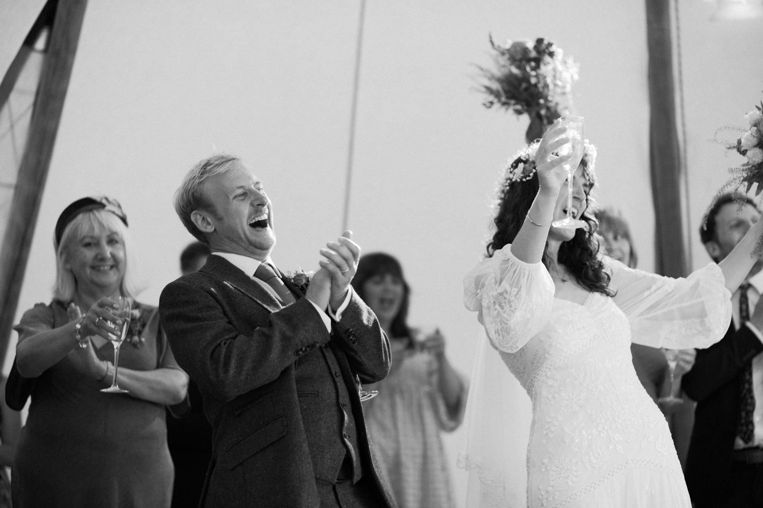 Hannah lifting her bouquet while guests applaud in the tipi