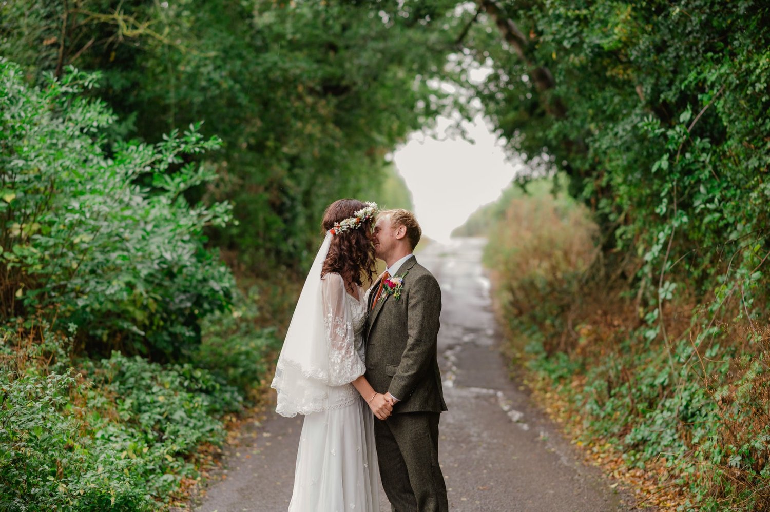 Hannah and Alex kissing beside green hedgerows on the lane