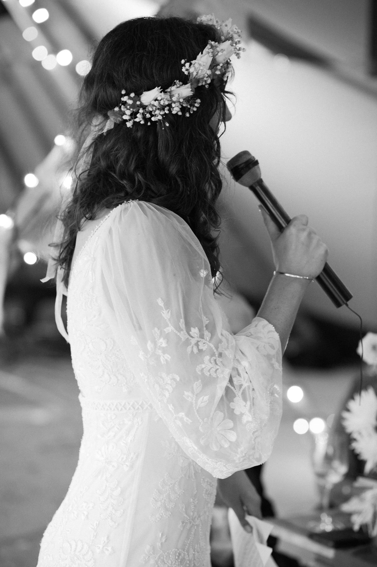 Hannah addressing guests with a microphone under string lights