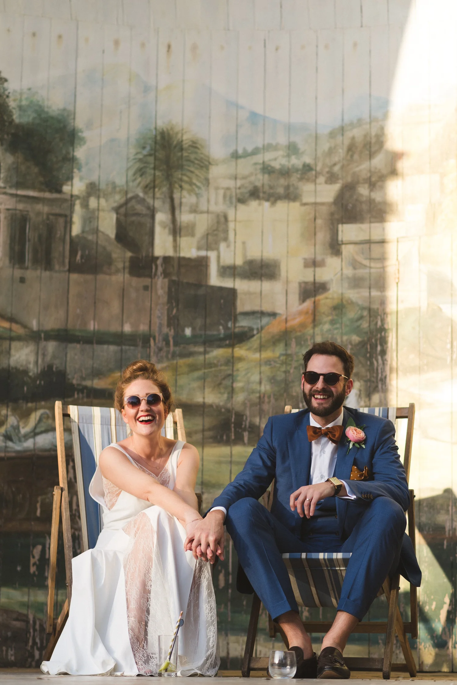 A smiling wedding couple sitting on deckchairs in the sunshine