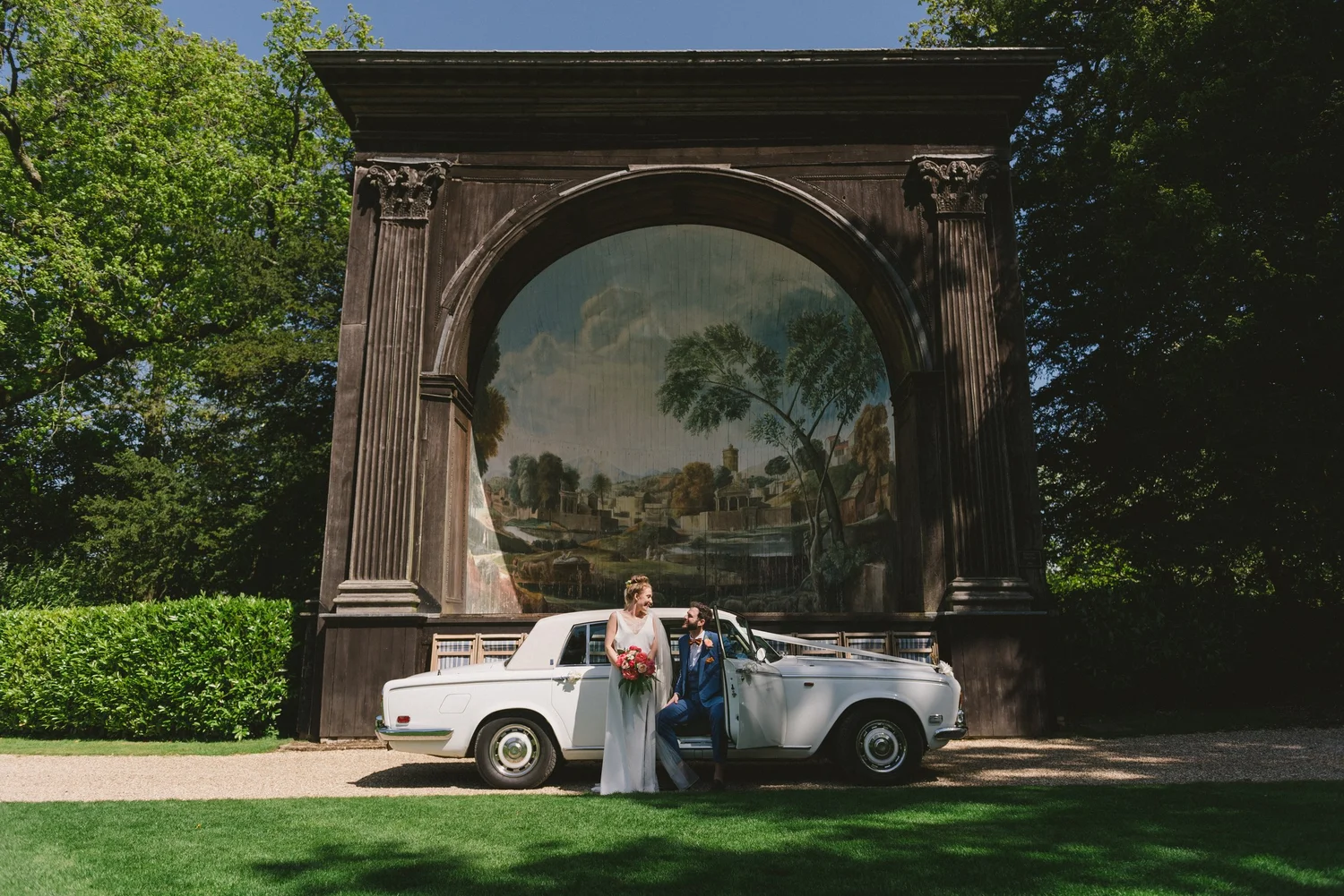 A bride and groom standing in front of a vintage white car